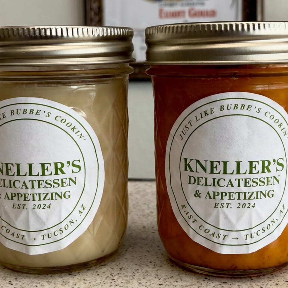 Two mason jars of pale and reddish condiments labeled Kneller’s Delicatessen & Appetizing sit on a speckled countertop.